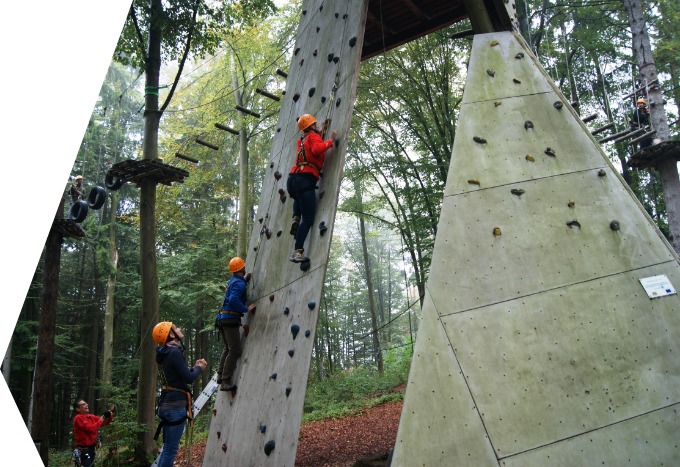 Personen an einer Kletterwand im Wald.